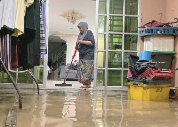 Mariati Mansor membersihkan rumahnya yang dimasuki air akibat fenomena air pasang besar di Kuala Kedah, semalam.