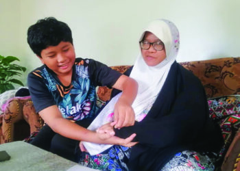 FIQBALL Iman  Firdaus membantu ibunya, Ramlah Andot yang lumpuh tangan kiri akibat serangan angin ahmar di rumah mereka di Kampung Bukit Kulim, Marang. – UTUSAN/NOOR HAYATI MAMAT