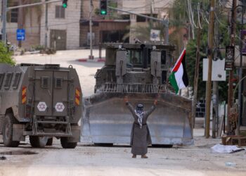 SEORANG aktivis Palestin mengangkat bendera negara ketika kenderaan berperisai dan jentolak Israel melalui jalan di Tulkarem, Tebing Barat.- AFP