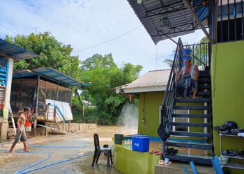 ABDUL Muin Ahmad  duduk di atas tangga loteng rumahnya  memerhatikan anak-anaknya mencuci lumpur akibat banjir di halaman rumahnya di Kampung Bawah Gunung, Baling, Kedah.