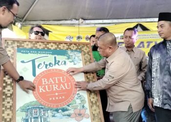 SAARANI Mohamad (kanan) meletakkan pelekat 'Batu Kurau' sempena Peluncuran Peta Eko Warisan Batu Kurau di Changkat Jering semalam. - UTUSAN/WAT KAMAL ABAS