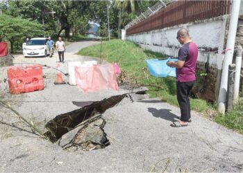 PENDUDUK Kampung Darat Kubur, Paka, Dungun di Terengganu meninjau keadaan jalan yang runtuh dan berlubang ekoran tanah mendap.– UTUSAN/NIK NUR IZZATUL HAZWANI NIK ADNAN