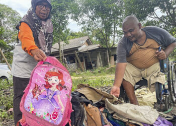 ZAINAL Abidin Kamarudin (kanan) dan isterinya menunjukkan beg terpakai yang rosak ditenggelami banjir di Kampung Padang, Kemasik di Kemaman, Terengganu.