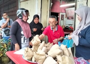 SITI Nurbaya Mohd. Zain (kanan) bersama bapanya ketika mengagihkan nasi bungkus percuma di kedainya di bandar Tumpat, Kelantan. – UTUSAN/ROHANA ISMAIL