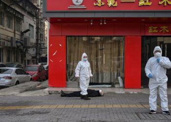 PEGAWAI berpakaian pelindung diri (PPE) memeriksa seorang lelaki yang rebah dan meninggal dunia di jalan berhampiran hospital di Wuhan, China.- AFP