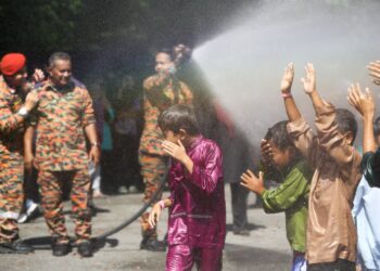 ANGGOTA bomba menyiram kanak-kanak yang menyertai program berkhatan di Kampung Chadak, Ulu Kinta di Ipoh hari ini. - UTUSAN/MUHAMAD