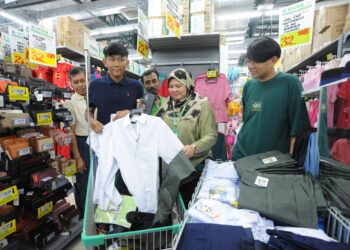 Pengurus Cawangan Econsave Taman Teratai Azian Mohd Yusof (dua dari kanan) membantu Mohamad Lutfi Muqri Mohamad Farok  dan  Mohamad Akmal Muqri membeli pakaian sekolah di Econsave Taman Teratai, Johor Bahru, semalam. – UTUSAN/RAJA JAAFAR ALI