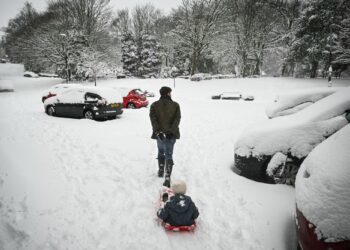 SEORANG lelaki menarik kanak-kanak yang duduk di atas kereta luncur melintasi taman yang dilitupi salji tebal di Marsden, utara England.-AFP