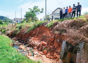 PENDUDUK menunjukkan keadaan runtuhan tebing berdekatan rumah yang semakin teruk di aman Puncak Bougainvillea di Kuala Kangsar semalam. – UTUSAN/FADZIL ZAINOL