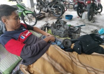 MOHAMAD Zulkarnain Mustafa yang lumpuh bahagian kaki ke bawah membaiki enjin motosikal dari atas katil ketika ditemui di Pasir Salak, Perak. – UTUSAN/AIN SAFRE BIDIN