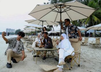 BEBERAPA pengunjung bergambar dengan berlatar belakang kemudahan payung pantai yang telah disediakan di Pantai Telok Kemang, Port Dickson.-UTUSAN/MOHD. SHAHJEHAN MAAMIN.