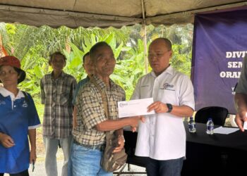 MUHAMMAD Olian Abdullah (kanan) menyampaikan dividen bagi bulan Disember kepada peserta Tanam Semula Komersial (TSK) Orang Asli Kampung Arung di Balai Raya Kampung Arung di Pekan, Pahang. - UTUSAN/NORHAFIZAN ZULKIFLI