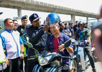 HUSSEIN Omar Khan mengagihkan topi keledar secara percuma kepada penunggang motosikal di Plaza Tol PJS2, Lebuhraya Baru Pantai (NPE) di sini hari ini.