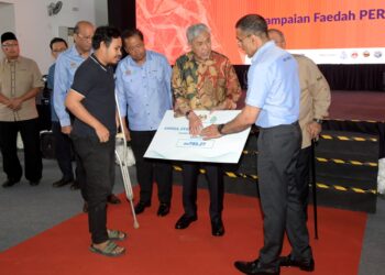 AHMAD Zahid Hamidi (tengah) menyampaikan skim faedah hilang upaya sementara Perkeso kepada Amirul Syahmi Mohd Nasoha (kiri) pada Karnival Kerjaya MyFutureJobs Bagan Datuk di Hutan Melintang hari ini. - UTUSAN/ZULFACHRI ZULKIFLI