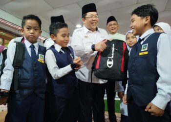 SIRAJUDDIN Suhaimee (tengah) menyerahkan beg kepada murid SK Menora sebagai simbolik melancarkan Kampung Angkat Madani Jakim di Kampung Menora Kuala Kangsar, Perak hari ini. - UTUSAN