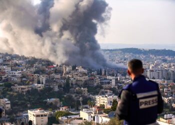 SEORANG wartawan melihat kepulan asap dari tapak serbuan Israel di kem pelarian Jenin di Tebing Barat.-AFP