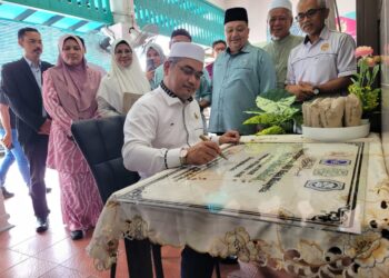 MOHD. Asri Mat Daud (tengah) menandatangani plak khas Majlis Penyampaian Sijil Perakuan Halal Malaysia Kepada Usahawan Nasi Berlauk Kak Chik di Kampung Berangan, Tumpat, Kelantan. - UTUSAN/MUSTAQIM MOHAMED