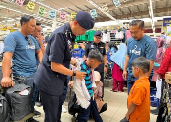 MOHD. Khairi Khairudin membantu kanak-kanak mengukur uniform dalam program kerjasama Polis Terengganu dengan sektor swasta dan pertubuhan bukan kerajaan (NGO) di Kuala Terengganu hari ini. - UTUSAN/KAMALIZA KAMARUDDIN