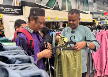 KADHAR Shah (kanan) membantu seorang warga OKU penglihatan memilih baju raya di pusat beli-belah di Bukit Mertajam, Pulau Pinang.-UTUSAN/SITI NUR MAS ERAH AMRAN