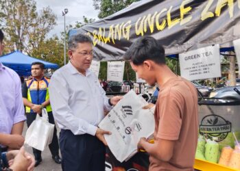 KHALID Mohamed (kiri) menyerahkan beg kempen kepada seorang peniaga di Bazar Ramadan MITC, Ayer Keroh, Melaka. – UTUSAN/MUHAMMAD SHAHIZAM TAZALI