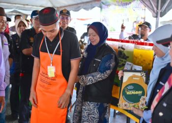 KASEMANI Embong (tengah) memakaikan apron kepada seorang peniaga di Bazar Ramadan Teluk Ketapang, Kuala Terengganu, semalam. - UTUSAN/KAMALIZA KAMARUDDIN