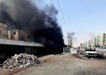 KEPULAN asap hitam kelihatan dari sebuah bangunan bersebelahan kereta yang rosak di tepi jalan di Khartoum. - AFP