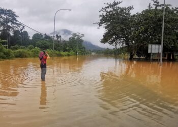 SEORANG wanita melihat lokasi yang dinaiki air di Jalan Dabong-Jeli dekat Jeli, Kelantan. - JKR JELI