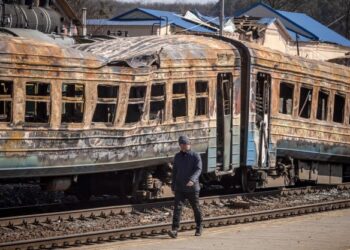 SEORANG lelaki berjalan melalui sebuah kereta api yang musnah akibat serangan bom Rusia di bandar timur laut, Trostianets, Ukraine. - AFP 