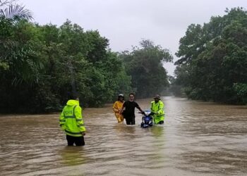 ANGGOTA IPD Pasir Mas membantu menolak motosikal Mohd. Faizal Zawawi yang terkandas dalam air banjir di Jalan Pasir Mas-Rantau Panjang hari ini. - UTUSAN/YATIMIN ABDULLAH