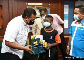 ABDUL Rahman Mohamad (kiri) menyampaikan sumbangan set pakaian seragam sekolah kepada seorang murid Orang Asli di SK Kechau 1, di Lipis, Pahang hari ini.