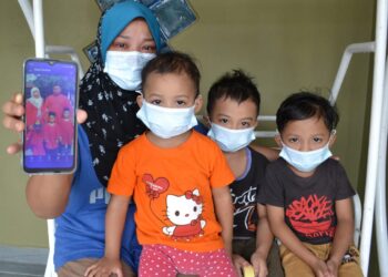 SITI Norhidayu Mohd. Nasir (kiri) bersama tiga orang anaknya melihat gambar kenangan bersama suami ketika ditemui di Taman Sri Ulu Bendul, Kuala Pilah, semalam. – UTUSAN/ZAKKINA WATI AHMAD TARMIZI