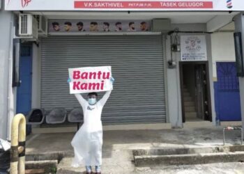 SEORANG tukang gunting memegang kadbod bertulis 'Bantu Kami' di hadapan sebuah kedai gunting rambut di Tasek Gelugor, Pulau Pinang.