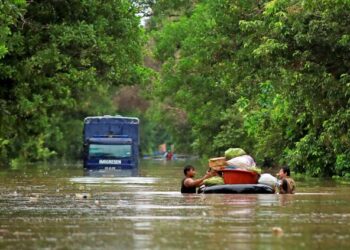 Dua penduduk kampung meredah banjir sedalam kira-kira satu meter sambil menolak pelampung dipenuhi barang di jalan Pasir Mas-Rantau Panjang Kelantan, semalam. – UTUSAN/KAMARUL BISMI KAMARUZAMAN.