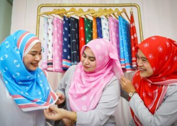 Di sebalik kemeriahan PRU15 dengan 945 calon, Nur Athirah Othman (kiri), Nuramiradiyana Zakaria (tengah) dan Nur Nihayatul Istiana Burhan teruja melihat tudung bercorak logo parti politik keluaran produk Kekaboo, di Batu Caves, semalam. – UTUSAN/SHIDDIEQIIN ZON