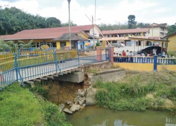 SEBILANGAN murid yang selesai sesi persekolahan tengah hari melihat lantai dan penahan konkrit tebing mulai runtuh di bawah jambatan Sungai Damak berdekatan pintu pagar masuk ke Sekolah Kebangsaan (SK) Damak di Jerantut, Pahang. – UTUSAN/HARIS FADILAH AHMAD