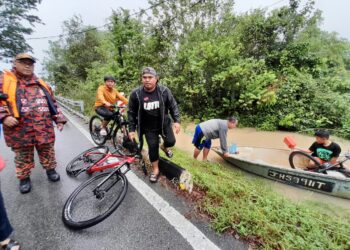 ANGGOTA bomba membantu Junaidi (baju hitam) yang menggunakan basikal meredah banjir dan hujan membeli bekalan makanan untuk keluarganya di Kampung Tembioh, Kota Tinggi.