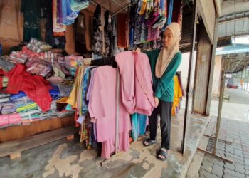 NOOR SHAFINA NAIM menunjukkan pakaian yang terjejas akibat banjir yang melanda kedai pakaian milik bapanya di Kota Tinggi.