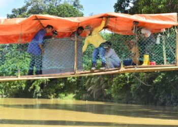 PENDUDUK kampung bergotong-royong membaiki jambatan gantung yang digunakan oleh penduduk Kampung Rekoh sebagai laluan utama bagi menghubungkan segala aktiviti harian mereka. – FOTO/SHAIKH AHMAD RAZIF