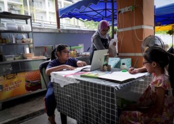 NUR Iman Zahra (kiri) dan Nur Iman Damia menjalani pengajaran dan pembelajaran di rumah (PDPr) di kediamannya sambil dipantau ibunya, Norazlina Jaafar yang berniaga burger. - UTUSAN/MOHD. FARIZWAN HASBULLAH