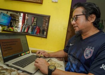 Peniaga pakaian terpakai, Nor Azman Abd Wahad meneliti syarat dan risiko yang bakal dihadapinya dari laman web sebuah bank sebelum  memohon moratorium pinjaman ketika ditemui  di Taman Lestari Perdana, Puchong, semalam. – UTUSAN/FARIZ RUSADIO