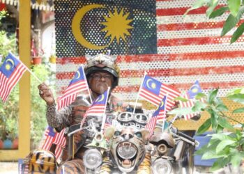 KHAMARUDIN Salleh dengan penuh semangat mengibarkan jalur gemilang bersama motosikal unik miliknya yang dihias kira-kira 30 bendera Malaysia di Taman Sri Serdang, Kepala Batas, Pulau Pinang, semalam. - FOTO/AMIR IRSYAD OMAR