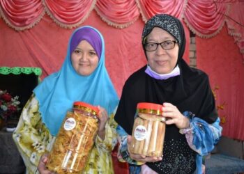 ROSLINAH A. Kadir bersama anaknya menunjukkan kerepek pisang dan kuih kapit yang dijual di Kampung Sungai Mahang, Nilai, Seremban. – UTUSAN/ZAKKINA WATI AHMAD TARMIZI