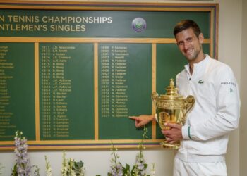 NOVAK Djokovic memegang trofi Wimbledon sambil menunjukkan namanya terpahat di papan Kemasyhuran semalam.