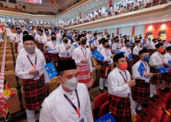 SEBAHAGIAN perwakilan Pemuda UMNO mengibarkan bendera ketika menyanyikan lagu UMNO pada Majlis Perasmian Persidangan Sayap Wanita, Pemuda dan Puteri sempena PAU 2021 di Dewan Merdeka, PWTC, Kuala Lumpur, semalam. – FOTO/MUHAMAD IQBAL ROSLI