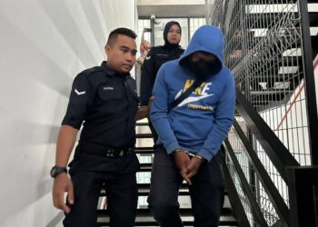 MOHD. Elfie Faizal Che Min (kanan) diringi anggota polis selepas didakwa atas pertuduhan meminta dan menerima rasuah sebanyak RM700 di Mahkamah Sesyen Ipoh hari ini. - UTUSAN