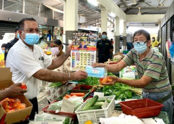 JAGDEEP Singh Deo (kiri) menyerahkan pelitup muka kepada peniaga di pasar awam Jalan Kuantan, Georgetown, Pulau Pinang hari ini.