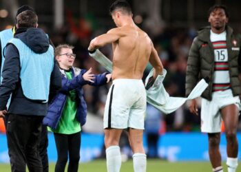 CRISTIANO Ronaldo membuka bajunya untuk diberikan kepada peminat cilik yang menceroboh padang dalam aksi kelayakan Piala Dunia 2022 di Stadium Aviva, Dublin semalam. – AFP