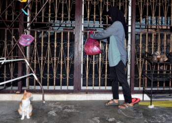 Hamiza Nazri menghantar bungkusan barang yang dipesan dengan  menggantungnya di pintu rumah  pelanggan dekat Kuala Pari Hilir, Ipoh, semalam. – UTUSAN/ZULFACHRI ZULKIFLI