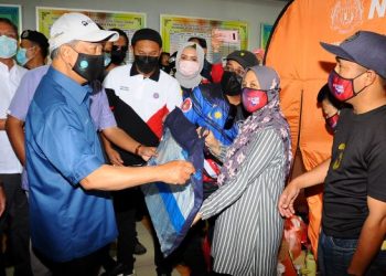 MUHYIDDIN Yassin menyampaikan bantuan kepada salah seorang mangsa banjir, Sueila Buti, 40, (dua dari kanan) bersama suaminya, Md. Hairul Othman, 39, (kanan) ketika mengadakan lawatan di PPS SK Laksamana, Kota Tinggi, Johor semalam. - FOTO/RAJA JAAFAR ALI