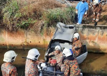 ANGGOTA bomba mengeluarkan lelaki dalam kereta yang terbabas masuk longkang di Seri Manjung hari ini. - UTUSAN/IHSAN JBPM PERAK